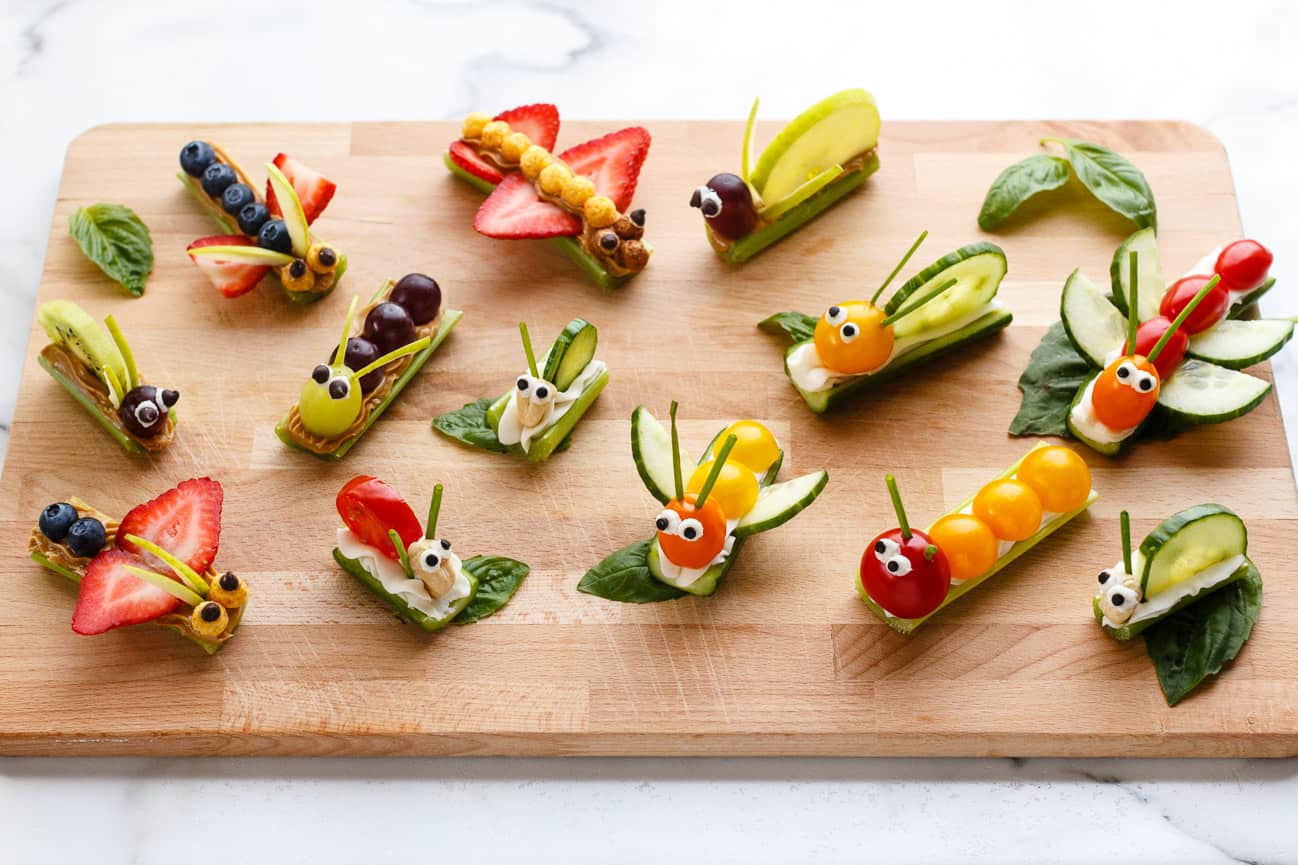 Fruit and vegetable bug snacks arranged on a wood board.