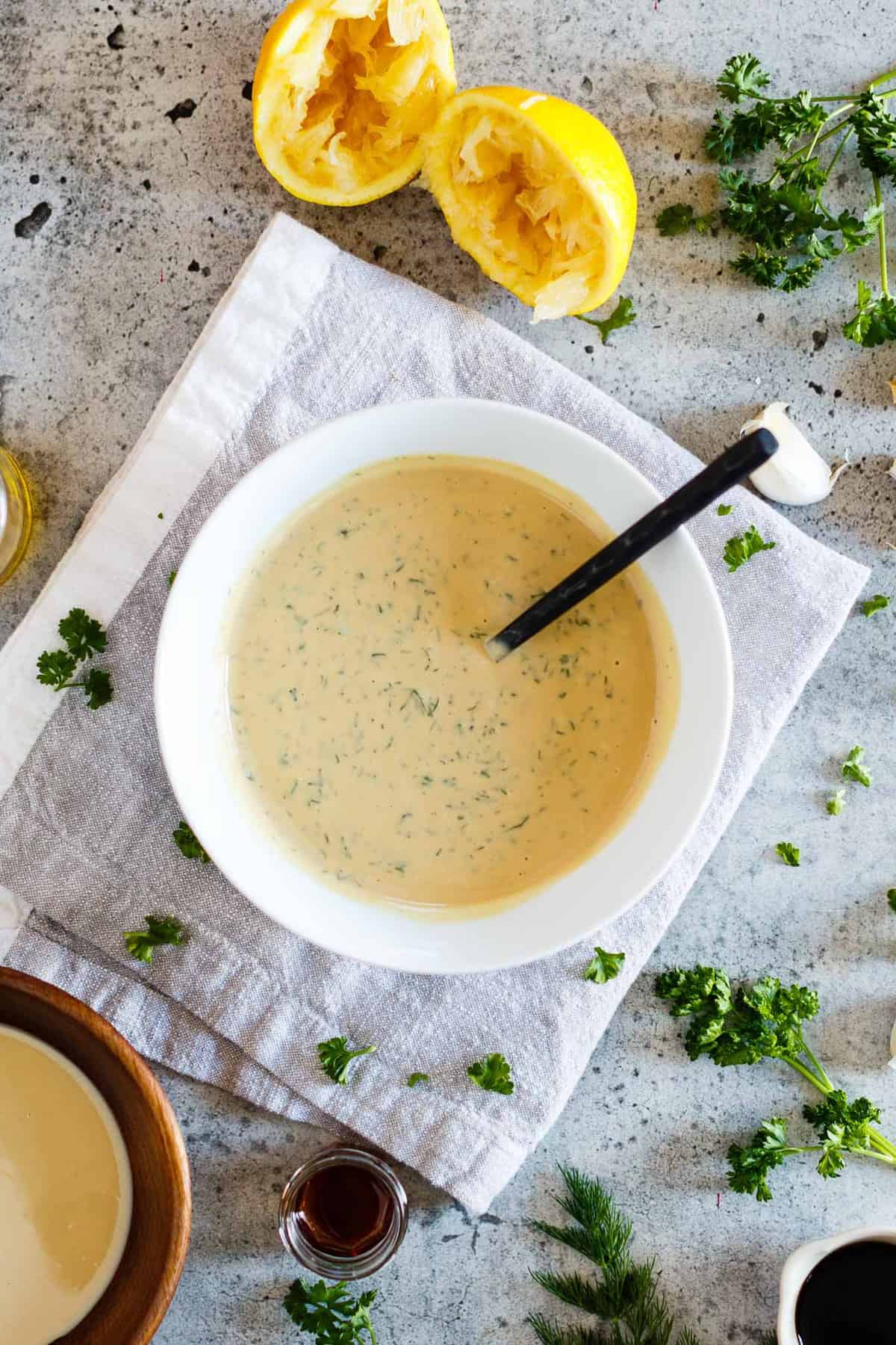 A bowl of Vegan Tahini Goddess Dressing surrounded by key ingredients on a concrete background.