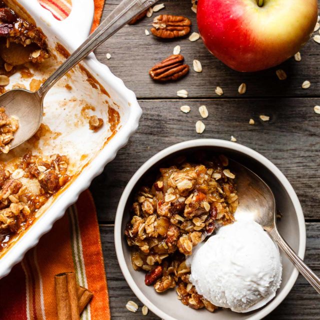 A bowl of vegan apple crisp served with a scoop of dairy-free vanilla ice cream.