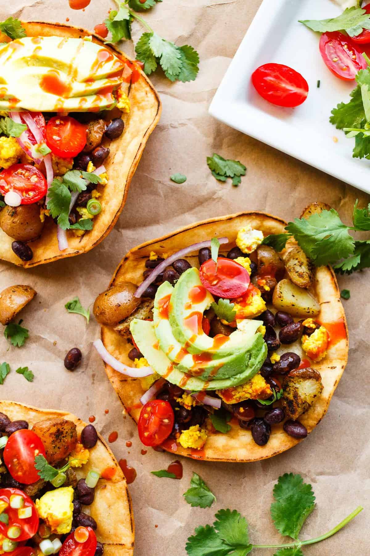 Vegan breakfast tostadas topped with avocado, hot sauce, tomtatoes, and cilantro.