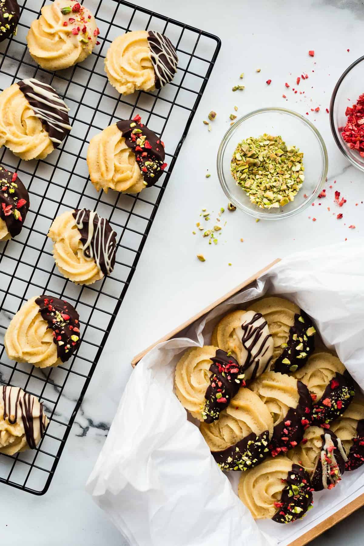Decorating vegan butter cookies with dark chocolate, crushed pistachios, and freeze-dried straberries/