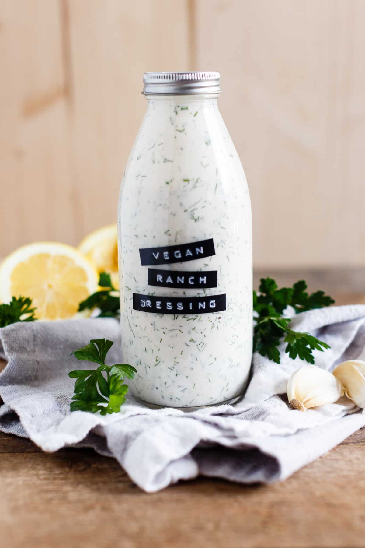 Bottle of homemade vegan ranch dressing shown on a grey kitchen towel and wood background.